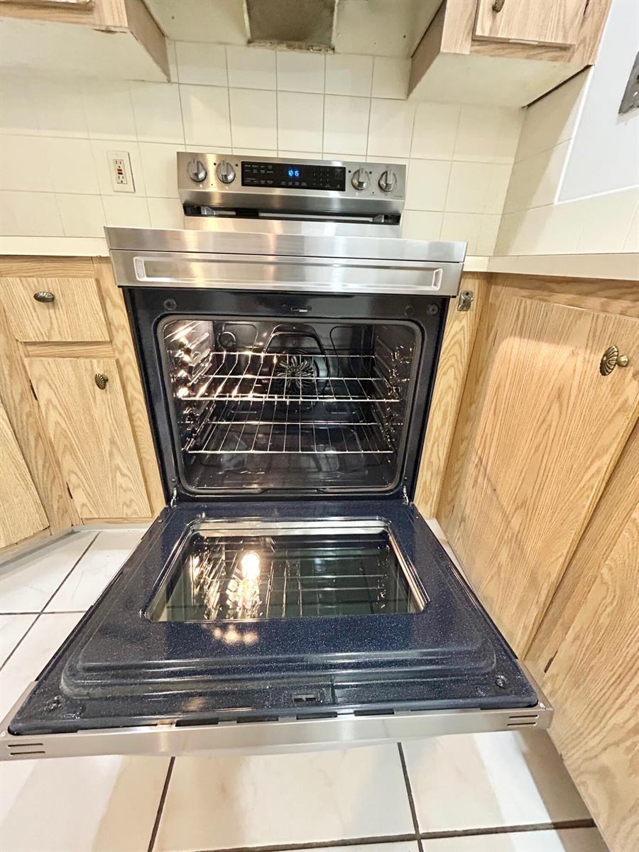 A stainless steel oven with an open door is centered between oak cabinets and tile — 433 Pine Glen Lane # C2, FL 33463, FL