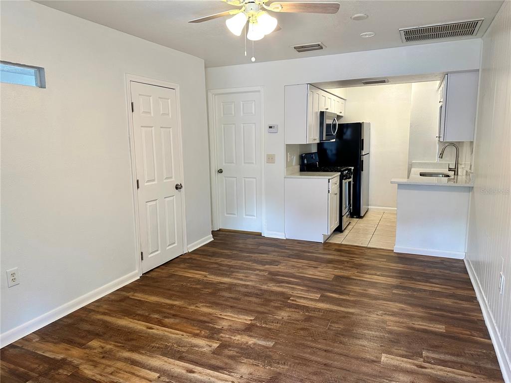 A room with wood-look flooring, a ceiling fan, two white doors, and an open kitchen — 1103 CYPRESS GARDENS BOULEVARD UNIT 51, WINTER HAVEN, FL