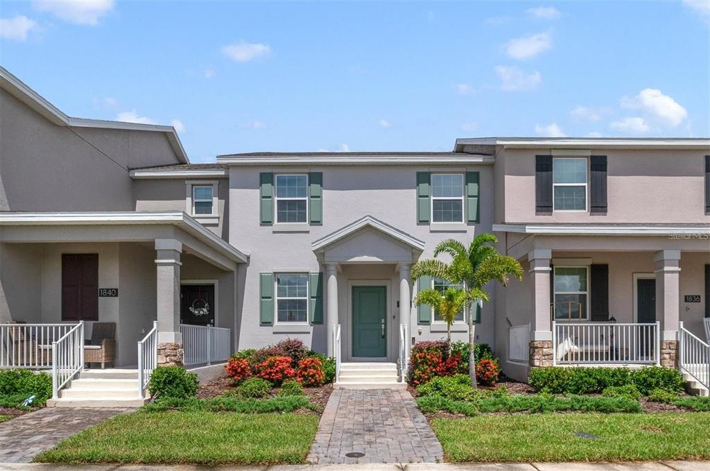 A two-story townhouse exterior features a central entrance, green shutters, and a paved walkway — 1838 TOHOQUA BOULEVARD, KISSIMMEE, FL