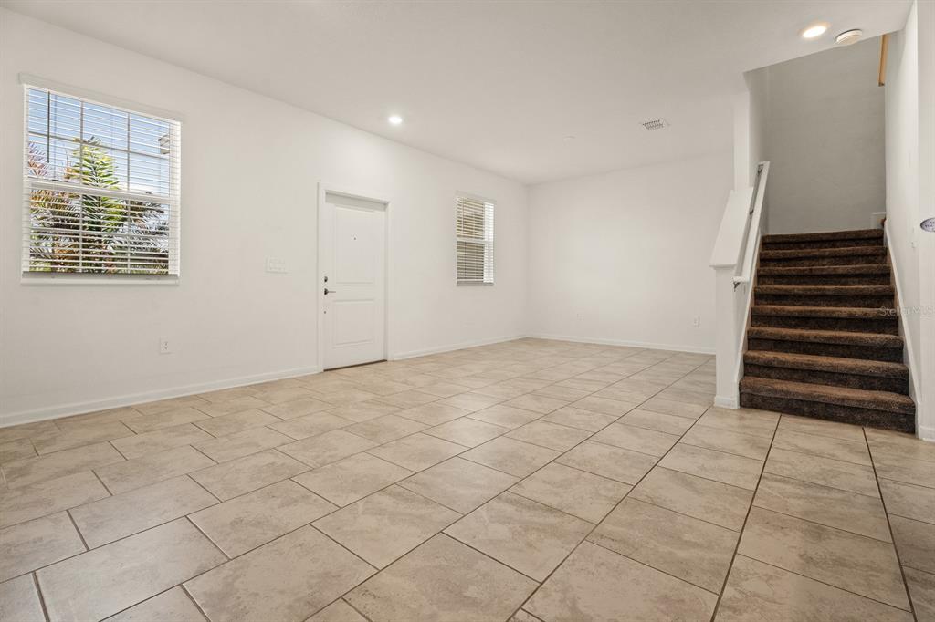 An empty room with light-colored tile flooring, white walls, a front door, and carpeted stairs — 1838 TOHOQUA BOULEVARD, KISSIMMEE, FL