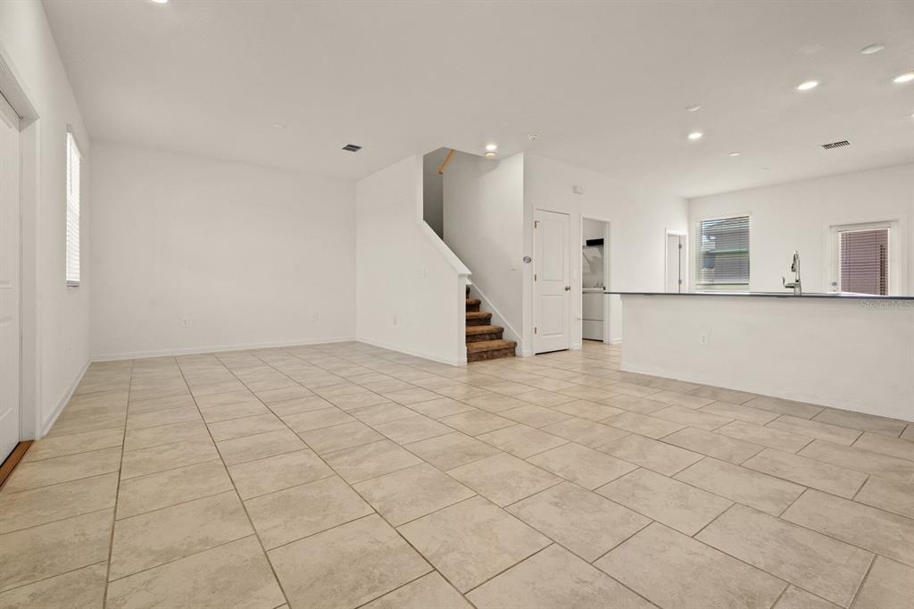An open-concept living area features light-colored tile flooring, white walls, and a carpeted staircase — 1838 TOHOQUA BOULEVARD, KISSIMMEE, FL