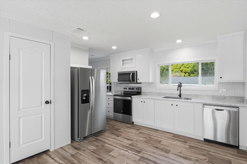 A kitchen with white cabinets, stainless steel appliances, a window, and wood-look flooring — 11421 RAMPART LANE, PORT RICHEY, FL