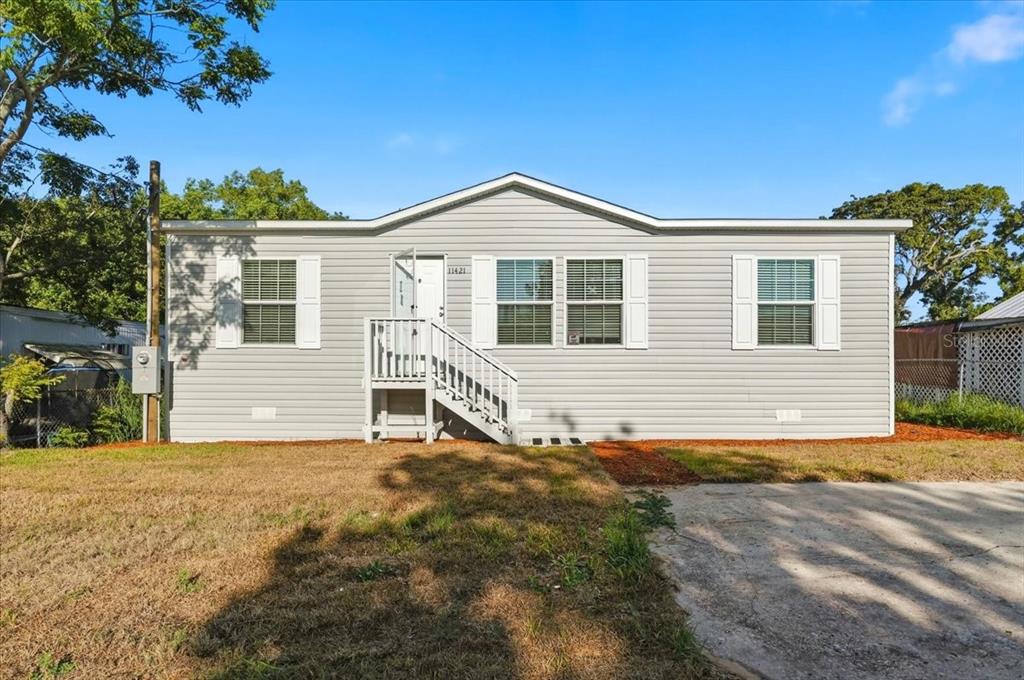 A single-story light gray house with white trim, a front porch, and a concrete driveway — 11421 RAMPART LANE, PORT RICHEY, FL