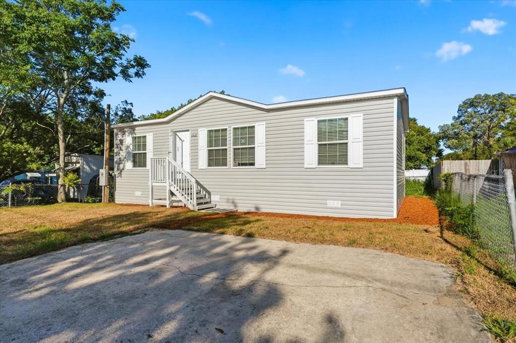 A light gray manufactured home with white trim and a concrete driveway under a blue sky — 11421 RAMPART LANE, PORT RICHEY, FL
