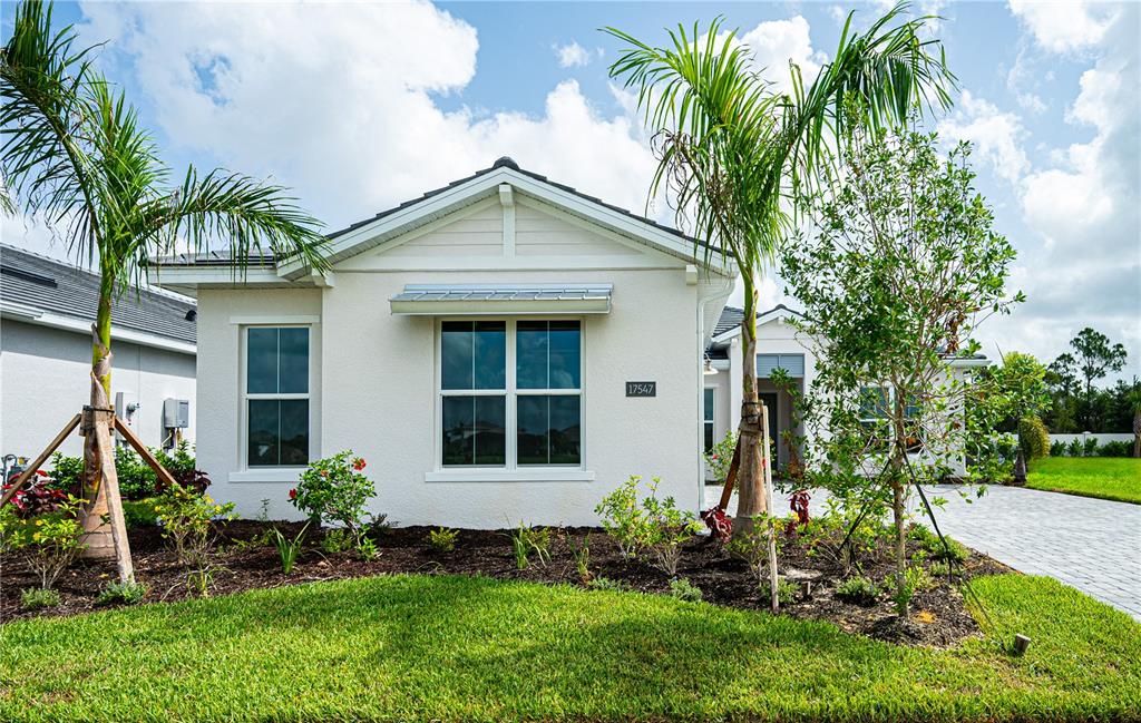 A single-story house with a light-colored stucco exterior, a metal awning, and two palm trees — 17547 PALMISTE DRIVE, BRADENTON, FL
