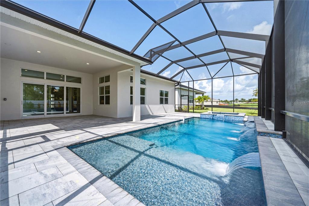 A swimming pool with water features and a spa sits inside a screened-in patio area — 17547 PALMISTE DRIVE, BRADENTON, FL