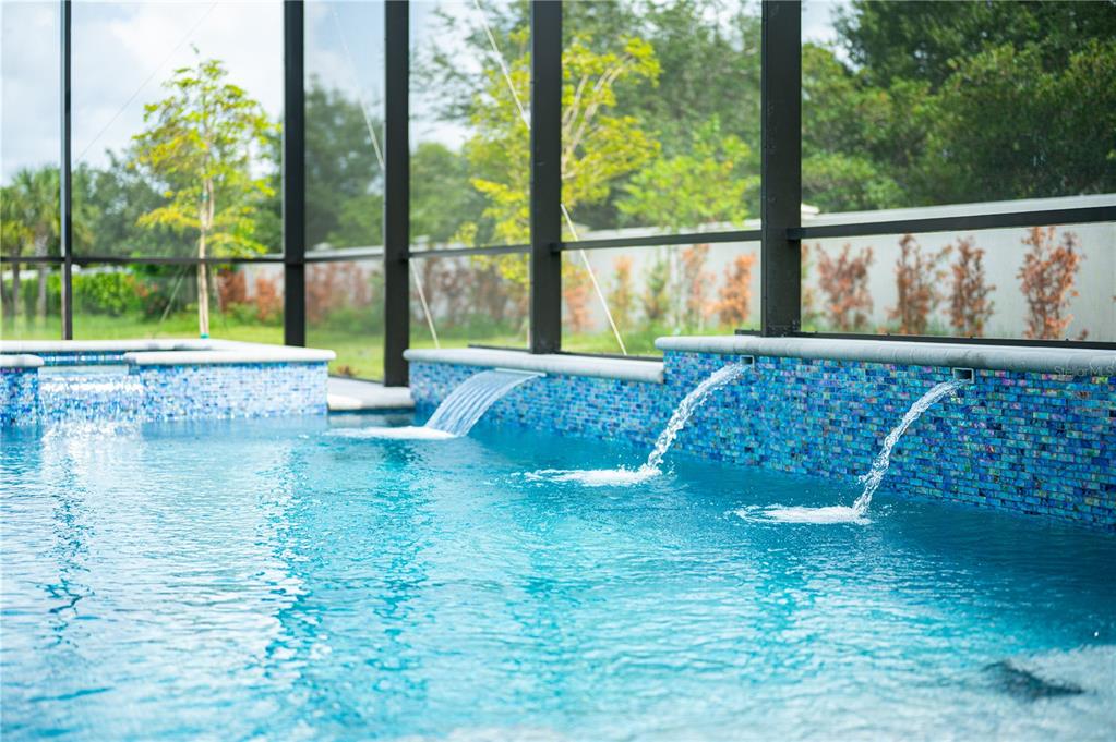 A swimming pool with three water features and blue mosaic tile walls inside a screened enclosure — 17547 PALMISTE DRIVE, BRADENTON, FL