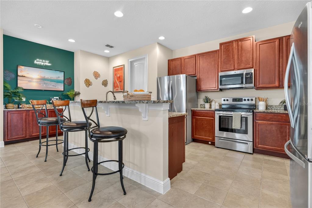 A kitchen features wood cabinets, stainless steel appliances, granite countertops, and a breakfast bar — 7639 WILMINGTON LOOP, KISSIMMEE, FL