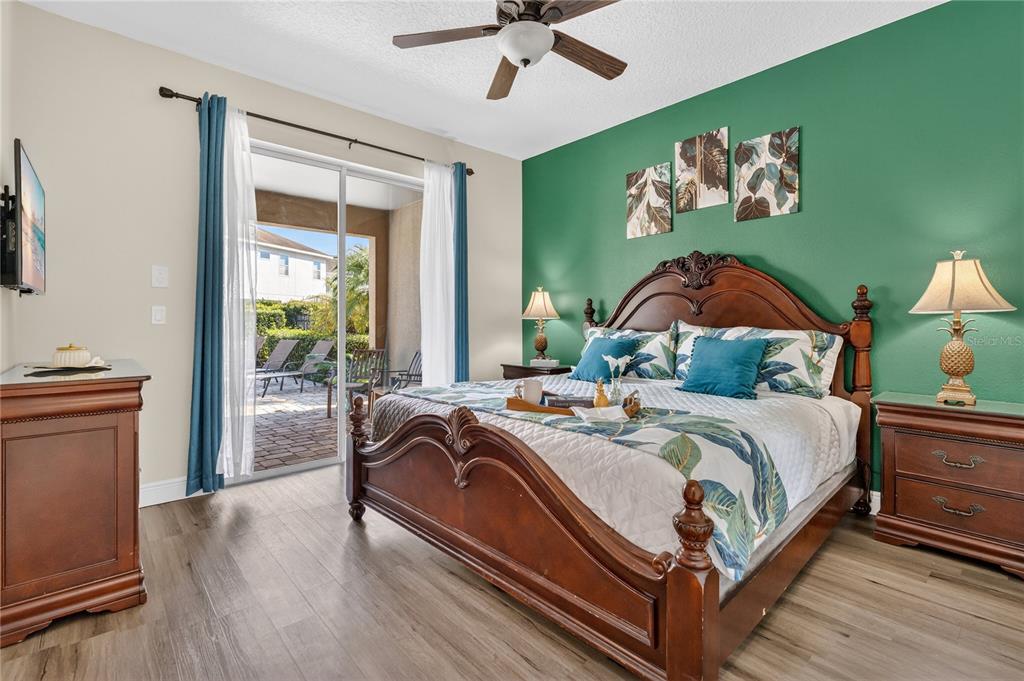 A bedroom features a wooden bed, green accent wall, and sliding glass doors to a patio — 7639 WILMINGTON LOOP, KISSIMMEE, FL