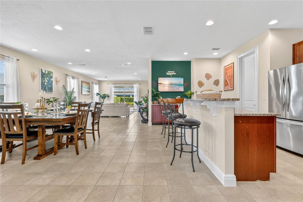An open-concept dining area and kitchen with tile flooring, bar seating, and a green accent wall — 7639 WILMINGTON LOOP, KISSIMMEE, FL
