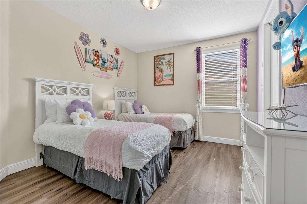 A bedroom features two twin beds with white headboards, wood-look flooring, and Lilo and Stitch decor — 7639 WILMINGTON LOOP, KISSIMMEE, FL