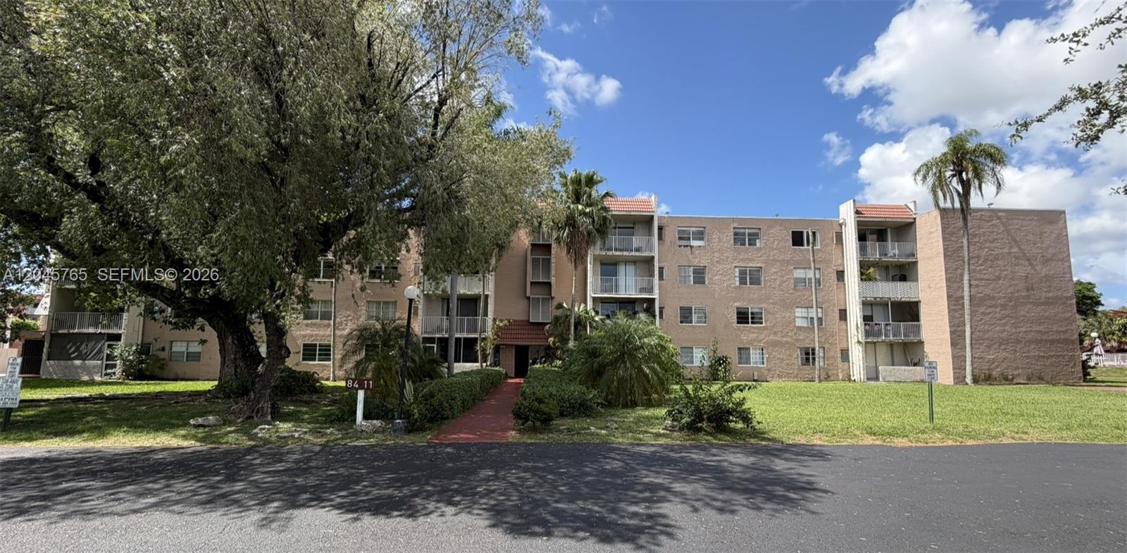 A multi-story tan apartment building with balconies stands behind a large tree and lawn — 8411 NW 8th St # 206, Miami FL 33126, MIAMI, FL
