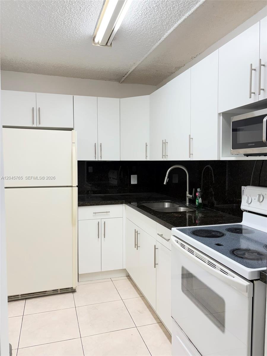 A kitchen features white cabinets, black countertops, a white refrigerator, and a white electric stove — 8411 NW 8th St # 206, Miami FL 33126, MIAMI, FL