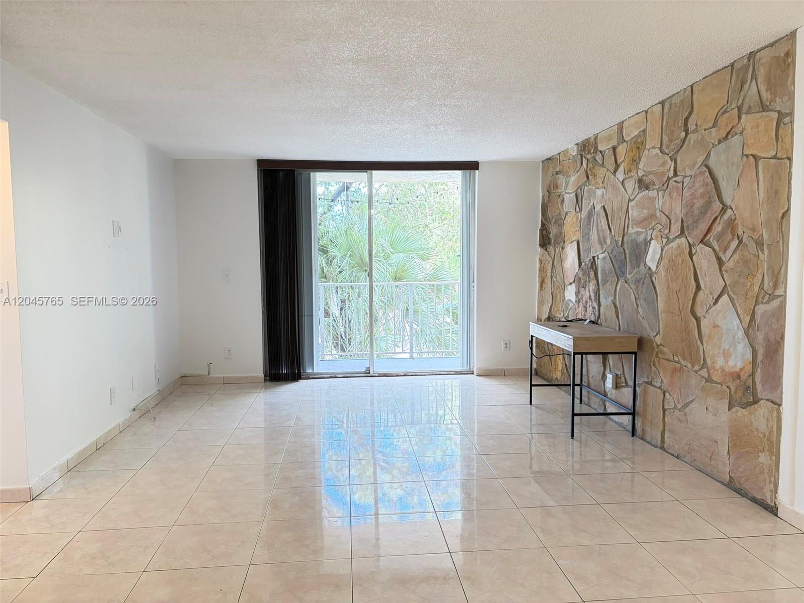 An empty room features light-colored tile flooring, white walls, and a prominent stone accent wall — 8411 NW 8th St # 206, Miami FL 33126, MIAMI, FL