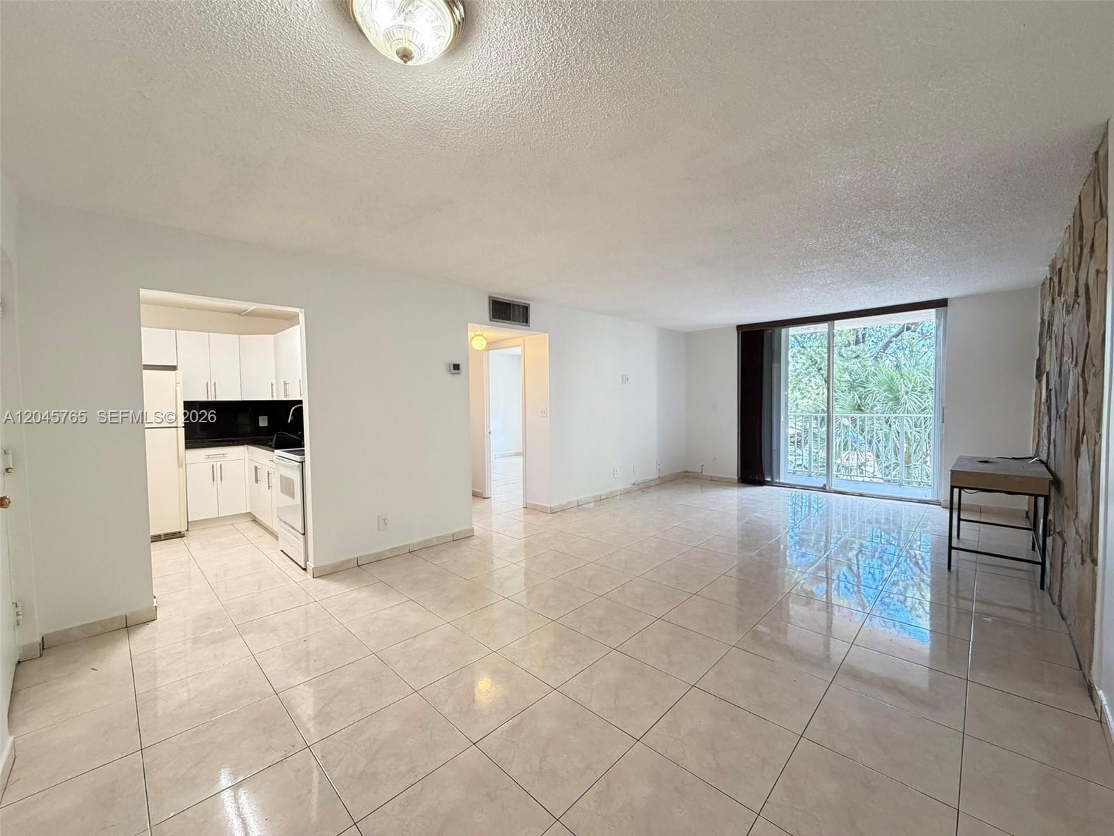 An open-concept living area features light tile flooring, a kitchen, and a stone accent wall — 8411 NW 8th St # 206, Miami FL 33126, MIAMI, FL