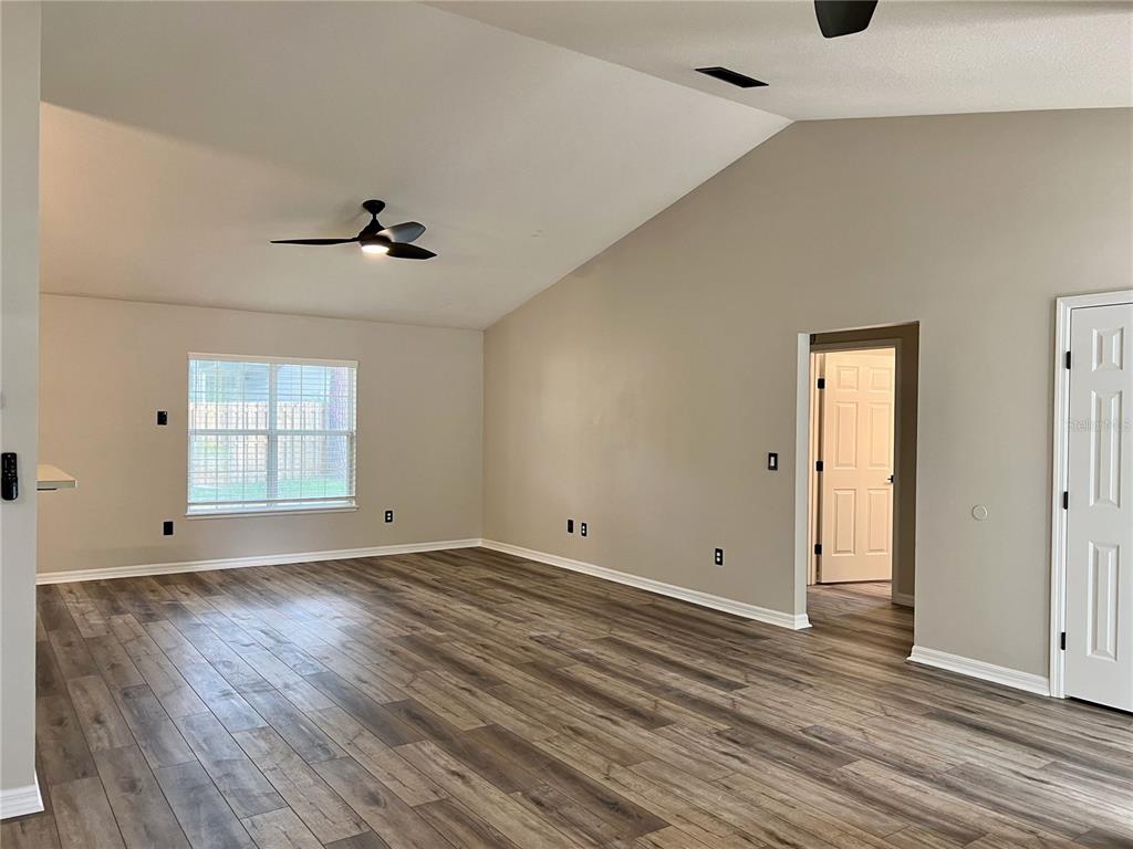 An empty living room features vaulted ceilings, a ceiling fan, and wood-look laminate flooring — 6845 SW 81ST STREET, GAINESVILLE, FL