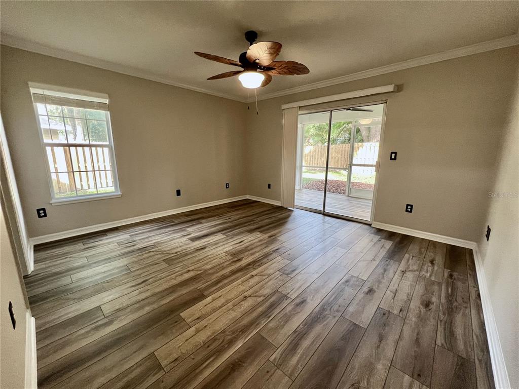 An empty room features wood-look flooring, a ceiling fan, a window, and sliding glass doors — 6845 SW 81ST STREET, GAINESVILLE, FL