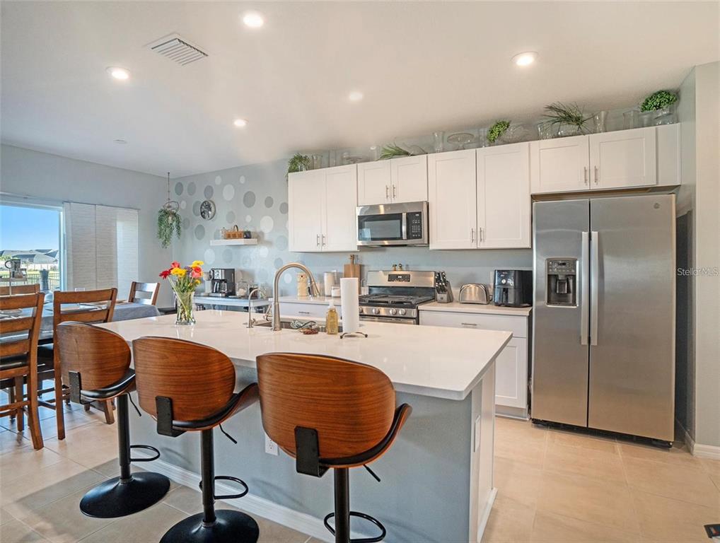 A kitchen features a white island with bar stools, stainless steel appliances, and white cabinetry — 5912 LAURELCREST GLEN, PALMETTO, FL