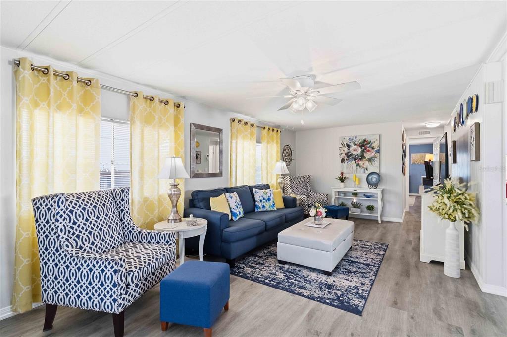 A living room features a blue sofa, patterned armchair, white ottoman, and yellow curtains — 2107 PALMA SOLA BOULEVARD UNIT 10, BRADENTON, FL