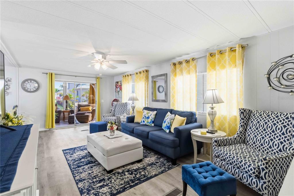 A living room features a blue sofa, patterned armchairs, a white ottoman, and yellow curtains — 2107 PALMA SOLA BOULEVARD UNIT 10, BRADENTON, FL