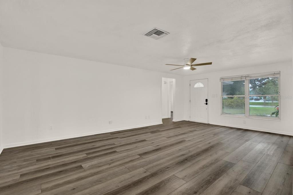 An empty living room features white walls, wood-look flooring, a ceiling fan, and a front door — 5995 BLOSSOM LAKE DRIVE, SEMINOLE, FL