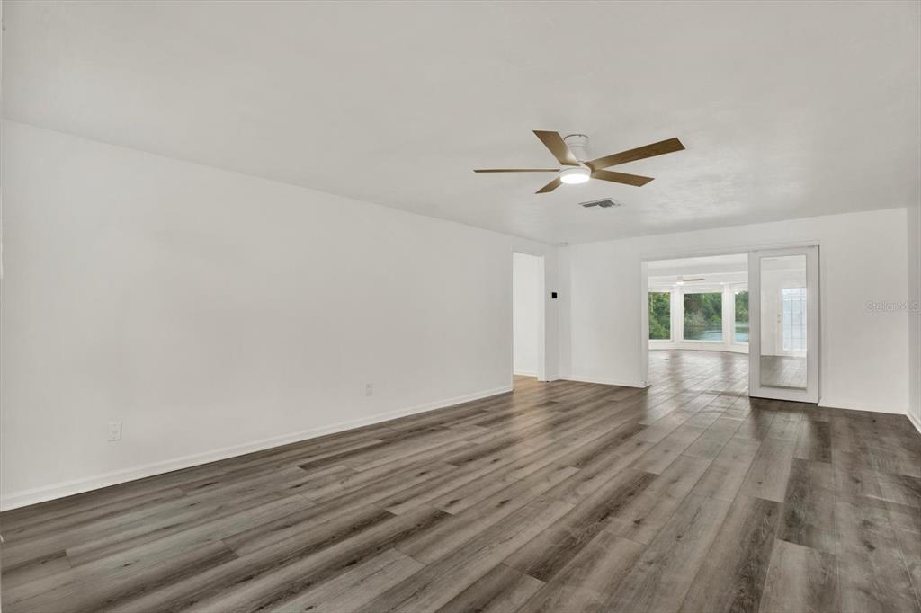 An empty room features white walls, wood-look flooring, a ceiling fan, and a glass door — 5995 BLOSSOM LAKE DRIVE, SEMINOLE, FL