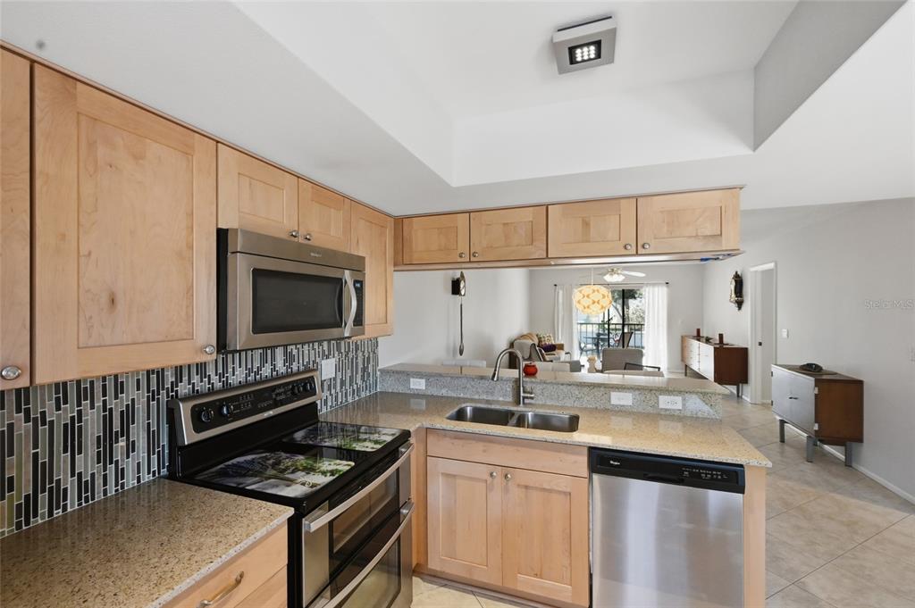 A kitchen with light wood cabinets, granite countertops, stainless steel appliances, and a tiled backsplash — 7845 EAGLE CREEK DRIVE, SARASOTA, FL