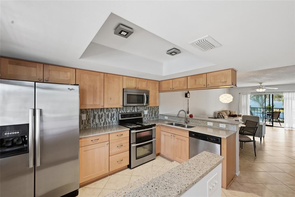 A kitchen with light wood cabinets, stainless steel appliances, and granite countertops opens to a living area — 7845 EAGLE CREEK DRIVE, SARASOTA, FL
