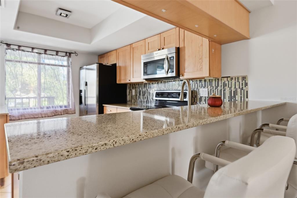A kitchen features light wood cabinets, granite countertops, stainless steel appliances, and a breakfast bar — 7845 EAGLE CREEK DRIVE, SARASOTA, FL