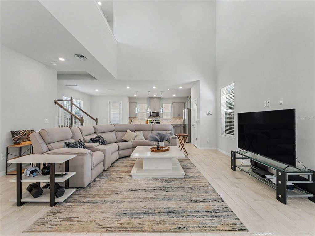 A spacious living room with a large sectional sofa, high ceilings, and an open kitchen — 13631 RANGELAND BOULEVARD, ODESSA, FL