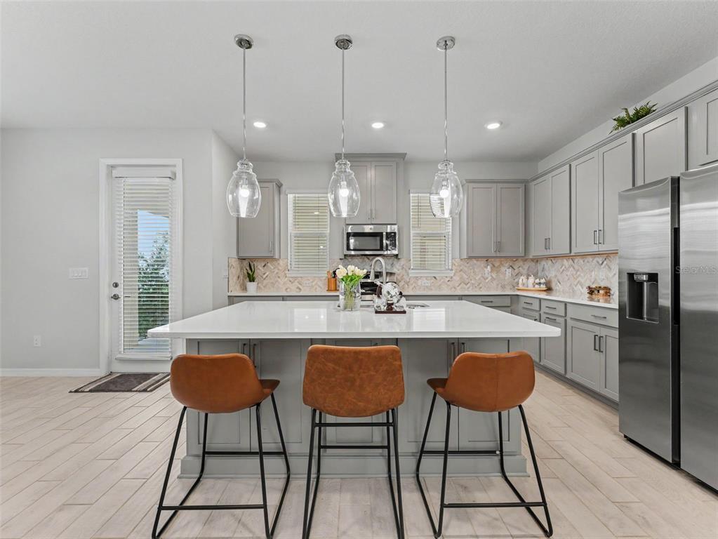 A modern kitchen features gray cabinetry, a white quartz island, and three glass pendant lights — 13631 RANGELAND BOULEVARD, ODESSA, FL