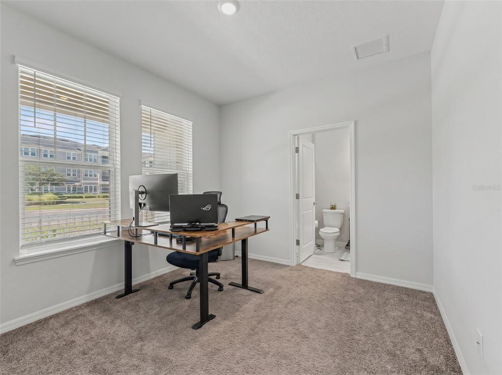 A home office with carpeted flooring, a desk, and an attached bathroom — 13631 RANGELAND BOULEVARD, ODESSA, FL