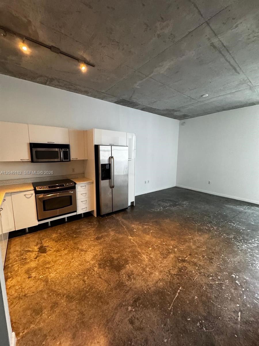 An industrial-style kitchen features white cabinets, stainless steel appliances, and exposed concrete ceilings and floors — 133 NE 2nd Ave # 904, Miami FL 33132, MIAMI, FL