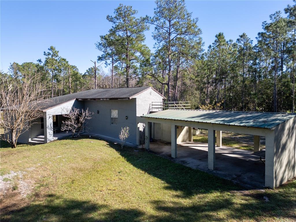 A gray house with a metal-roofed carport sits on a grassy lot near pine trees — 10411 COUNTY ROAD 474, CLERMONT, FL