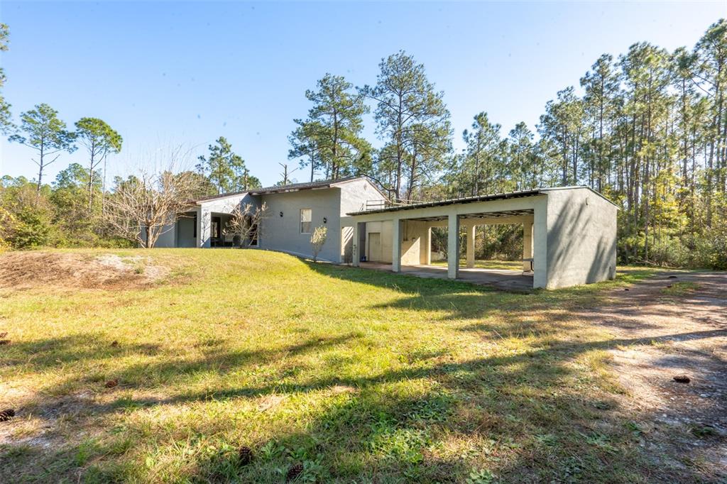 A gray house with an attached carport sits on a grassy lot near pine trees — 10411 COUNTY ROAD 474, CLERMONT, FL