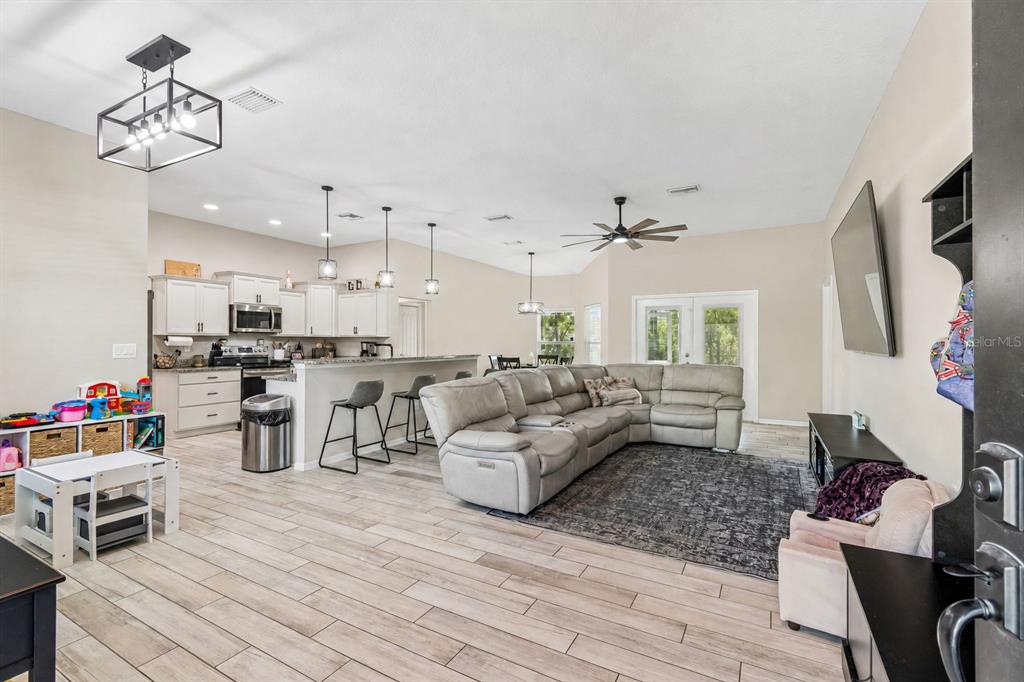 An open-concept living room and kitchen featuring light wood-look tile flooring and a sectional sofa — 15476 MULHATTON ROAD, WEEKI WACHEE, FL
