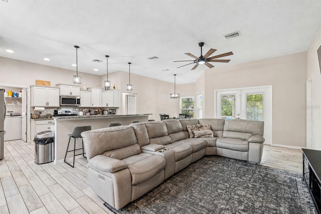 A spacious open-concept living room features a large sectional sofa, kitchen island, and tile flooring — 15476 MULHATTON ROAD, WEEKI WACHEE, FL