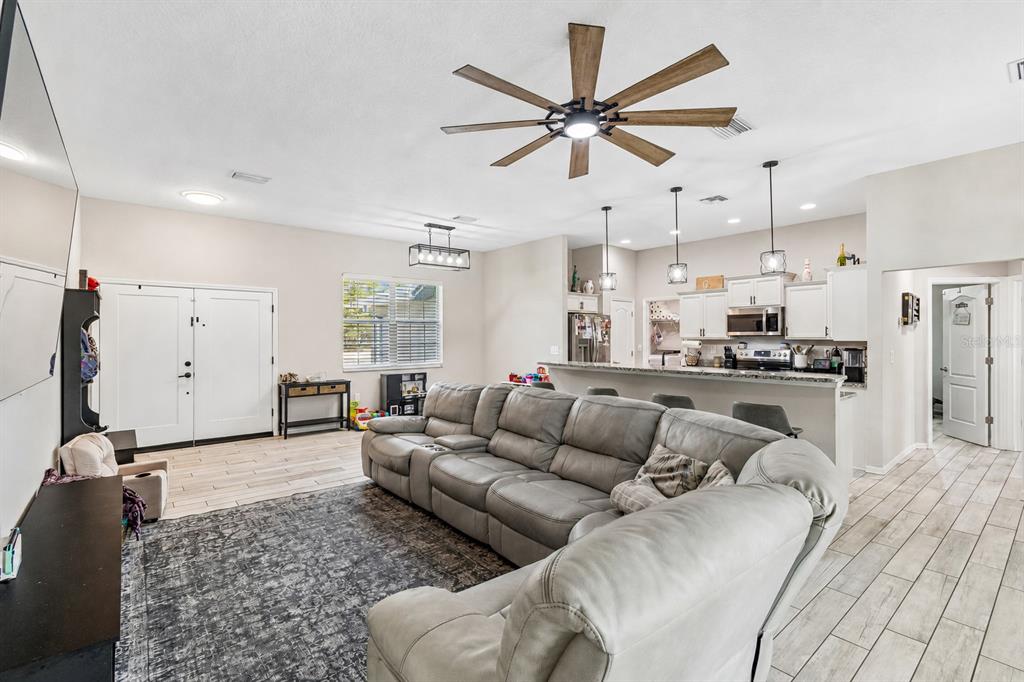 A spacious open-concept living room features a large gray sectional, tile flooring, and kitchen area — 15476 MULHATTON ROAD, WEEKI WACHEE, FL