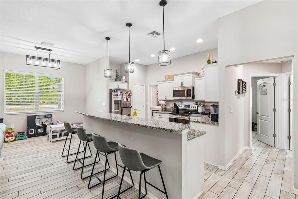A kitchen features a granite-topped breakfast bar, gray stools, and light-colored tile flooring — 15476 MULHATTON ROAD, WEEKI WACHEE, FL