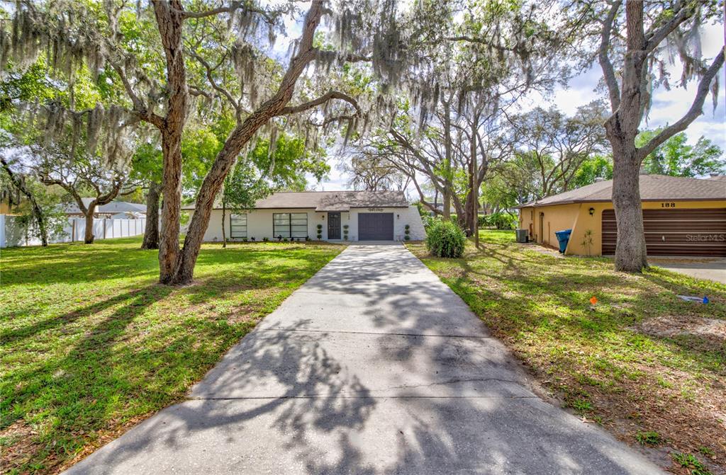 A white single-story house with a concrete driveway and large trees in the front yard — 198 TULSA AVENUE, SPRING HILL, FL