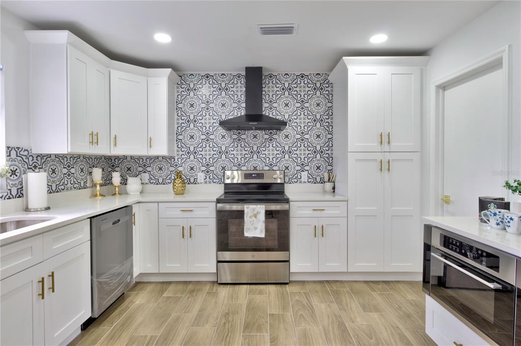 A kitchen features white cabinets, gold hardware, stainless steel appliances, and a patterned tile backsplash — 198 TULSA AVENUE, SPRING HILL, FL