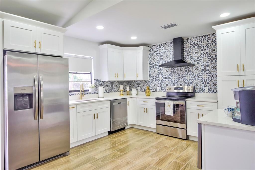 A kitchen features white cabinetry, stainless steel appliances, and a patterned blue and white backsplash — 198 TULSA AVENUE, SPRING HILL, FL
