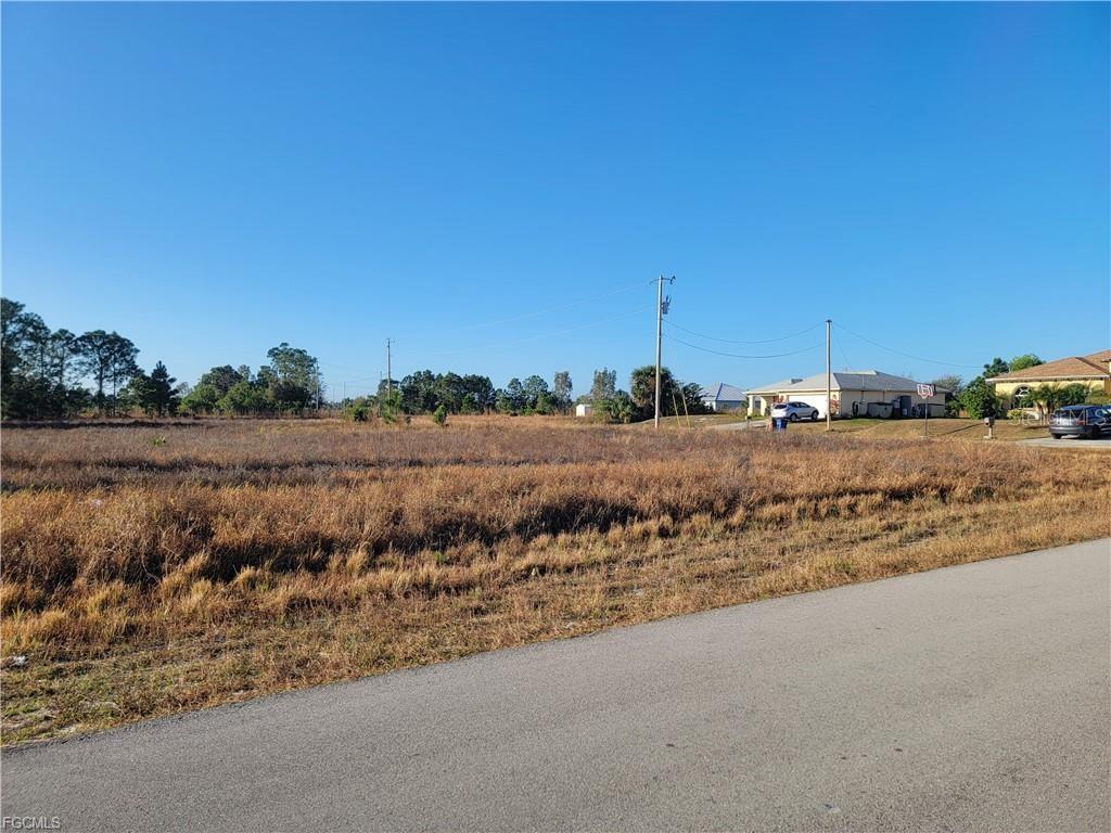 A vacant, grassy lot sits next to a paved road and a suburban house — 707 FRONTENAC AVENUE S, LEHIGH ACRES, FL