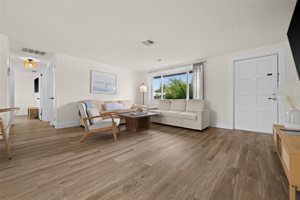 A living room with light wood-look flooring, two sofas, an armchair, and a white front door — 219 CORAL ROAD, VENICE, FL