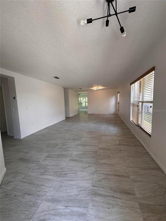 A spacious, empty room features light gray tile flooring, white walls, and a modern chandelier — 4502 PHILADELPHIA CIRCLE, KISSIMMEE, FL