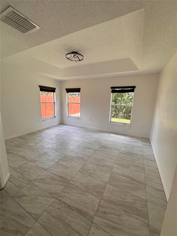 An empty room features light-colored tile flooring, a tray ceiling, and three windows — 4502 PHILADELPHIA CIRCLE, KISSIMMEE, FL