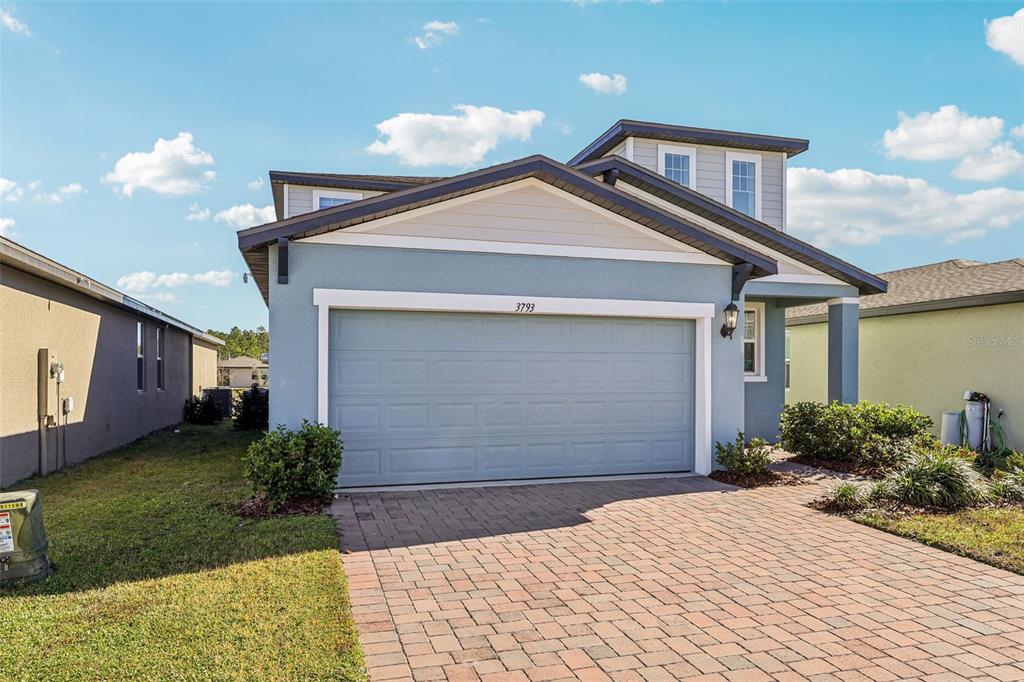 A blue suburban house features a two-car garage and a brick paver driveway — 3793 BLUETHREAD WAY, POINCIANA, FL