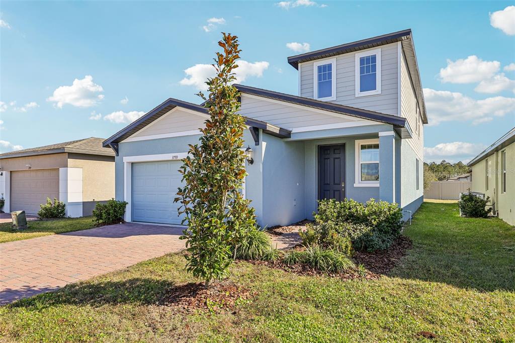 A two-story house with light blue stucco, a front-facing garage, and a small front yard — 3793 BLUETHREAD WAY, POINCIANA, FL