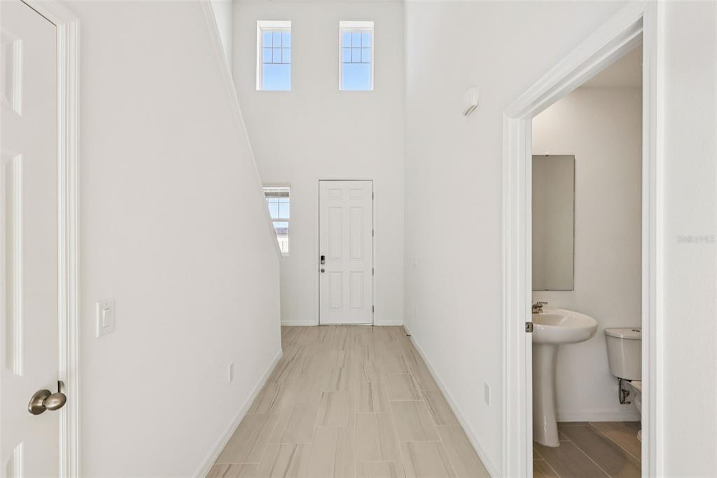 A bright entryway with high ceilings, light tile flooring, a front door, and a half bathroom — 3793 BLUETHREAD WAY, POINCIANA, FL