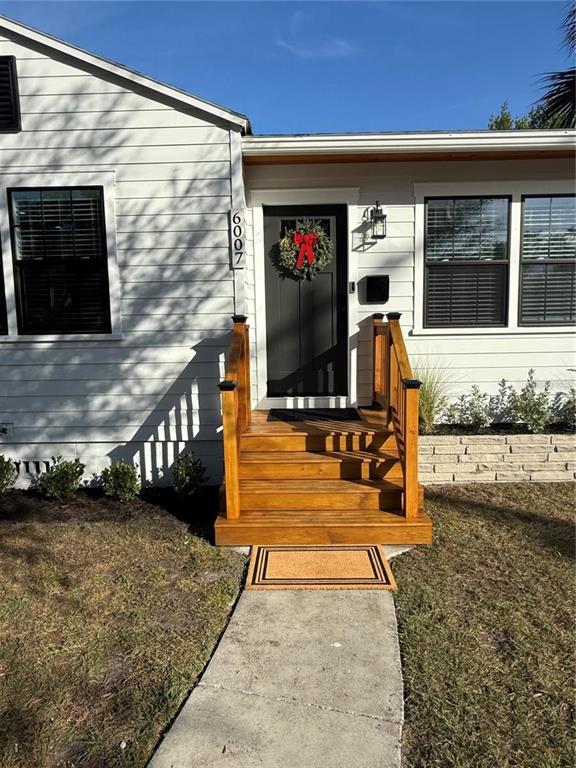 The exterior of a white house features a dark front door with a wooden staircase — 6007 N CENTRAL AVENUE, TAMPA, FL